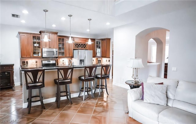 kitchen with hanging light fixtures, a kitchen breakfast bar, dark tile patterned floors, stainless steel appliances, and decorative backsplash