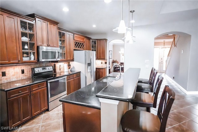 kitchen with sink, a center island with sink, stainless steel appliances, light tile patterned flooring, and decorative light fixtures