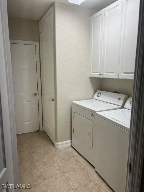 clothes washing area with cabinets, washing machine and clothes dryer, and light tile patterned floors