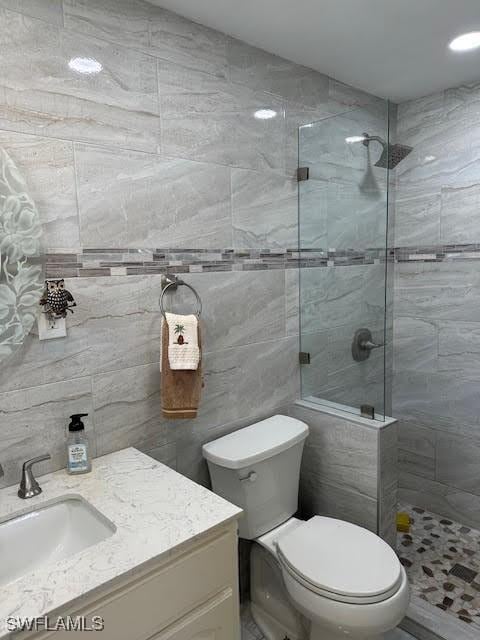 bathroom with vanity, tiled shower, tile walls, and toilet