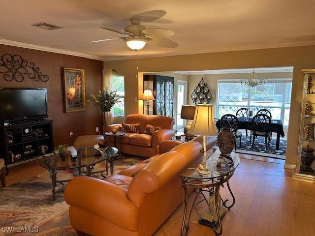 living room with crown molding, ceiling fan with notable chandelier, a wealth of natural light, and hardwood / wood-style floors