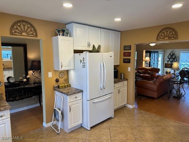 kitchen with white cabinetry, white fridge, light tile patterned floors, and dark stone counters