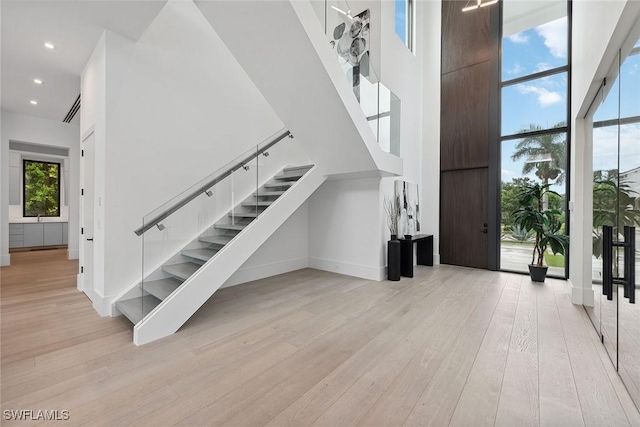 stairway featuring a towering ceiling, wood-type flooring, and a wall of windows