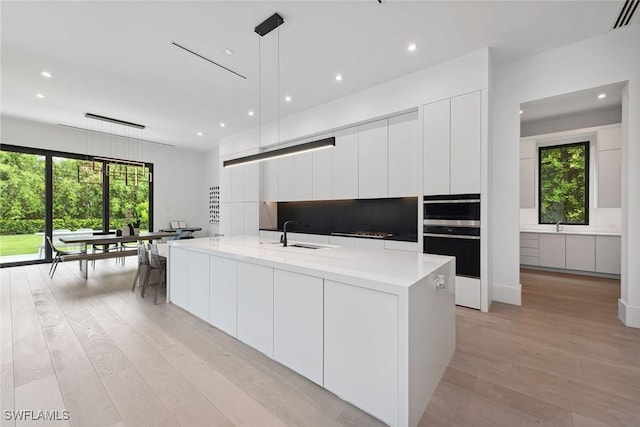 kitchen with a healthy amount of sunlight, decorative light fixtures, light hardwood / wood-style flooring, and white cabinets