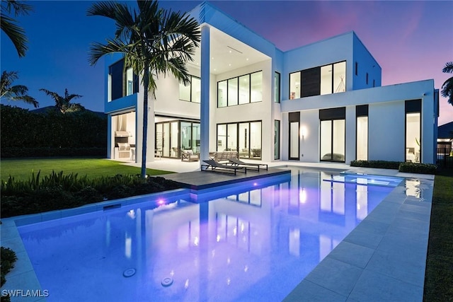 pool at dusk featuring a patio area and a lawn