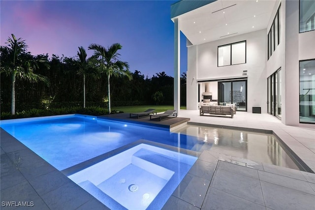 pool at dusk with outdoor lounge area and a patio