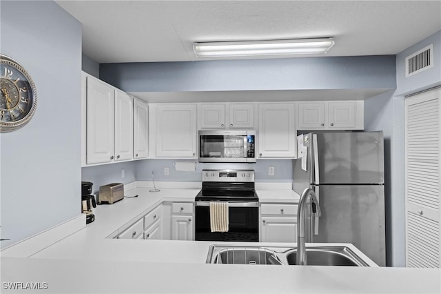 kitchen with white cabinetry, sink, stainless steel appliances, and kitchen peninsula