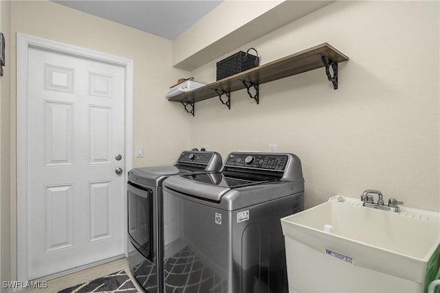 clothes washing area with sink, washing machine and clothes dryer, and light wood-type flooring