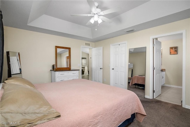 carpeted bedroom with ceiling fan, connected bathroom, and a raised ceiling