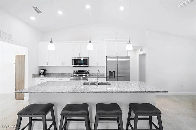 kitchen featuring sink, hanging light fixtures, stainless steel appliances, light stone countertops, and a center island with sink