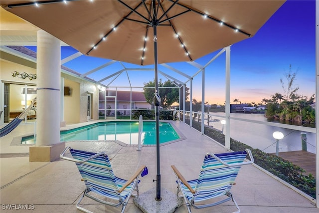 pool at dusk featuring a lanai, a patio area, and a water view