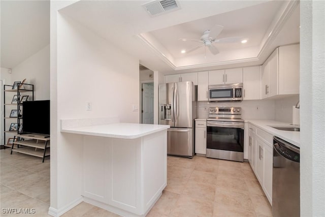 kitchen with appliances with stainless steel finishes, a tray ceiling, kitchen peninsula, ceiling fan, and white cabinets