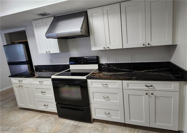 kitchen featuring stainless steel refrigerator, white cabinets, dark stone counters, electric range, and wall chimney exhaust hood