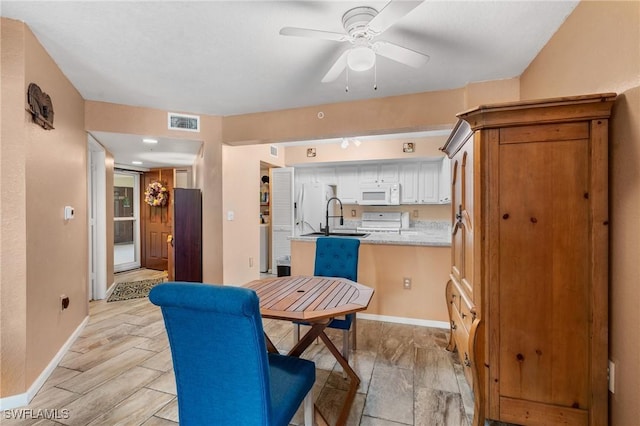 kitchen with sink, white appliances, kitchen peninsula, ceiling fan, and white cabinets