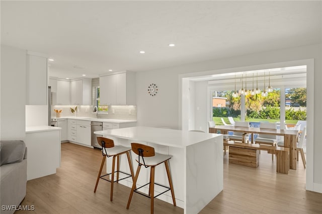 kitchen with decorative light fixtures, tasteful backsplash, dishwasher, white cabinets, and light hardwood / wood-style flooring