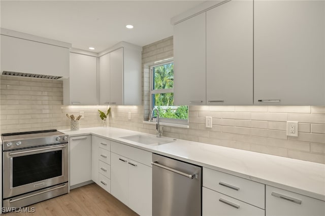 kitchen featuring white cabinetry, sink, decorative backsplash, stainless steel appliances, and light hardwood / wood-style flooring