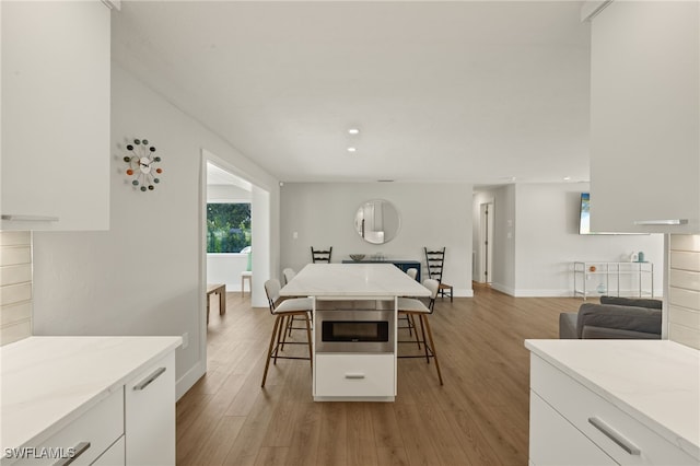 kitchen featuring a breakfast bar, light wood-type flooring, a kitchen island, and white cabinets