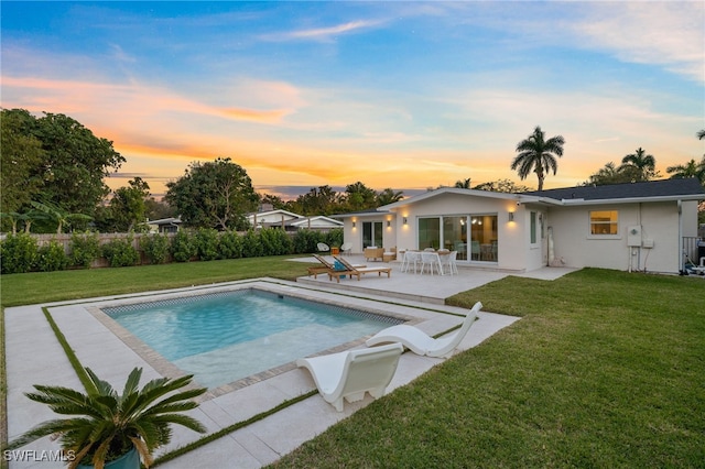 pool at dusk with a patio area and a lawn