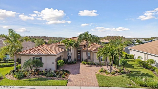 mediterranean / spanish home with decorative driveway, a tile roof, and a front lawn