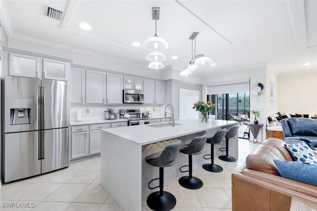 kitchen with light tile patterned flooring, appliances with stainless steel finishes, decorative light fixtures, sink, and a kitchen island with sink