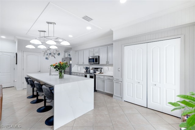 kitchen with gray cabinetry, hanging light fixtures, stainless steel appliances, and a center island with sink