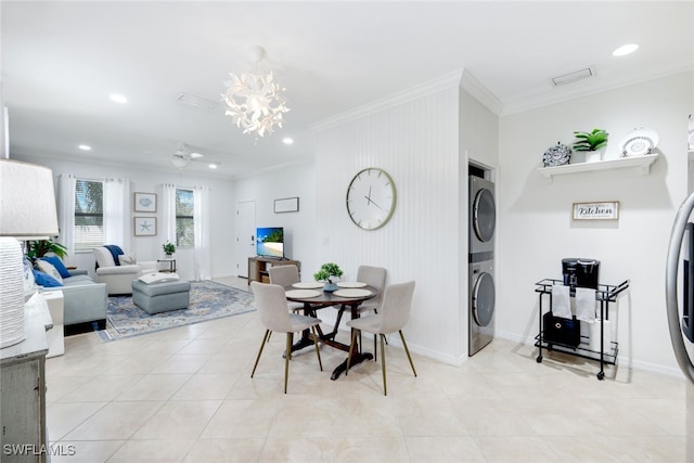 dining area with stacked washer and dryer, ornamental molding, light tile patterned flooring, and an inviting chandelier