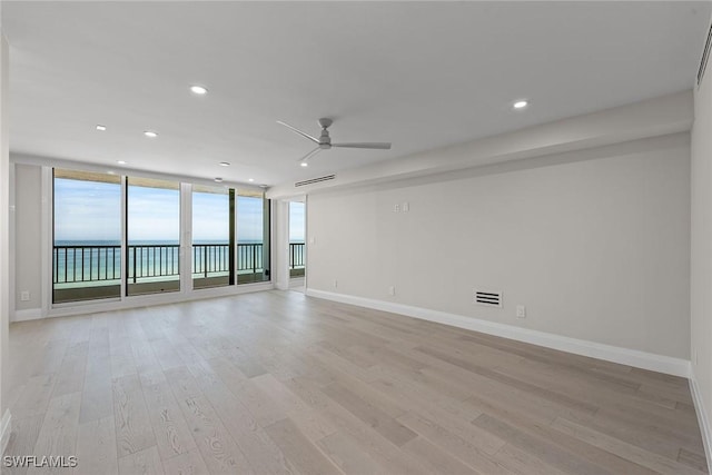 spare room with a water view, ceiling fan, expansive windows, and light wood-type flooring