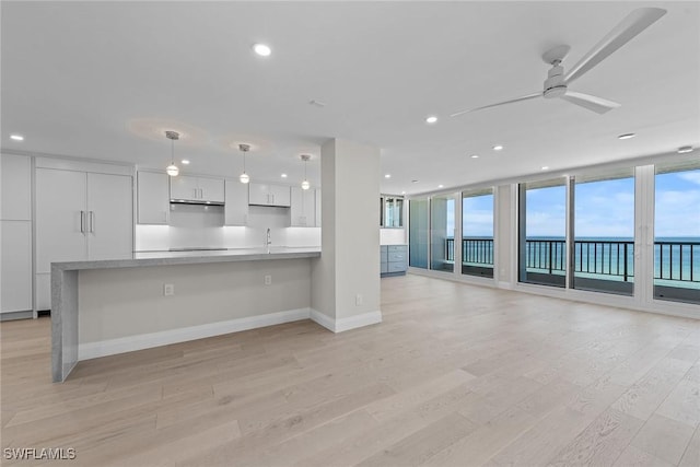 kitchen with white cabinets, hanging light fixtures, expansive windows, a water view, and light wood-type flooring