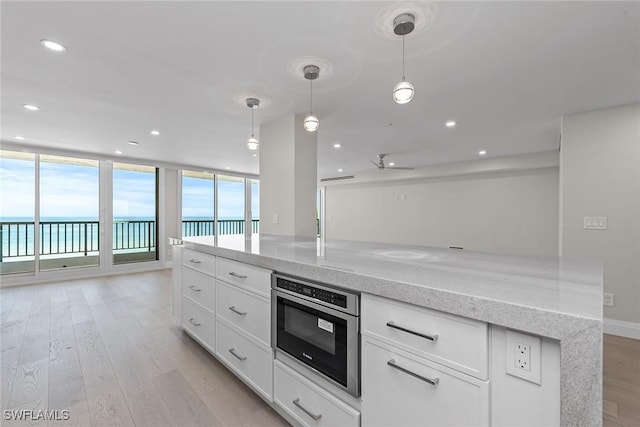 kitchen with a water view, white cabinetry, hanging light fixtures, light hardwood / wood-style flooring, and light stone countertops