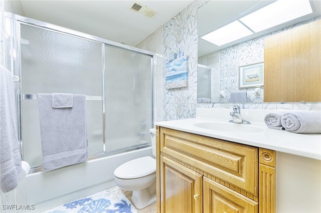 full bathroom with vanity, a skylight, shower / bath combination with glass door, and toilet