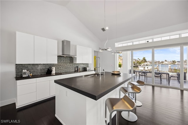 kitchen with pendant lighting, white cabinetry, sink, a kitchen island with sink, and wall chimney range hood