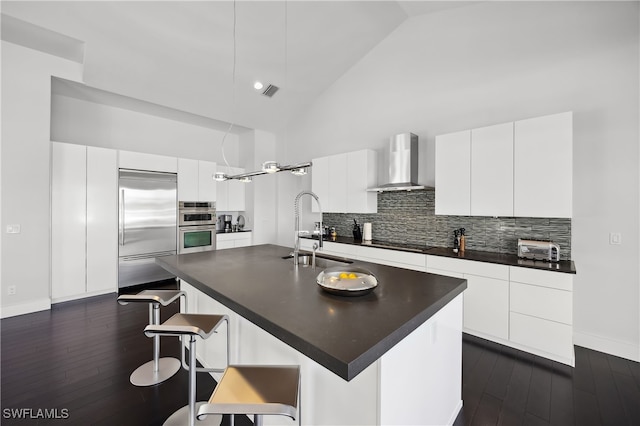 kitchen featuring sink, white cabinetry, stainless steel appliances, an island with sink, and wall chimney exhaust hood