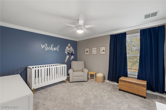 bedroom featuring crown molding, a nursery area, ceiling fan, and carpet flooring