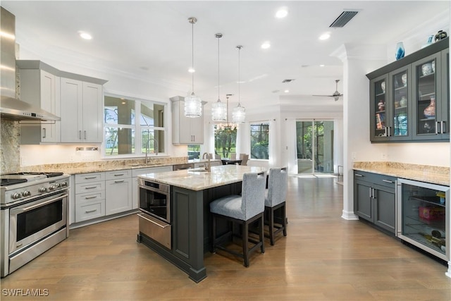 kitchen featuring light stone counters, stainless steel stove, a sink, beverage cooler, and wall chimney exhaust hood