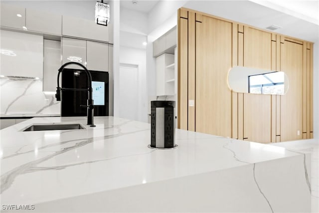 room details featuring white cabinetry, light stone countertops, sink, and light brown cabinetry