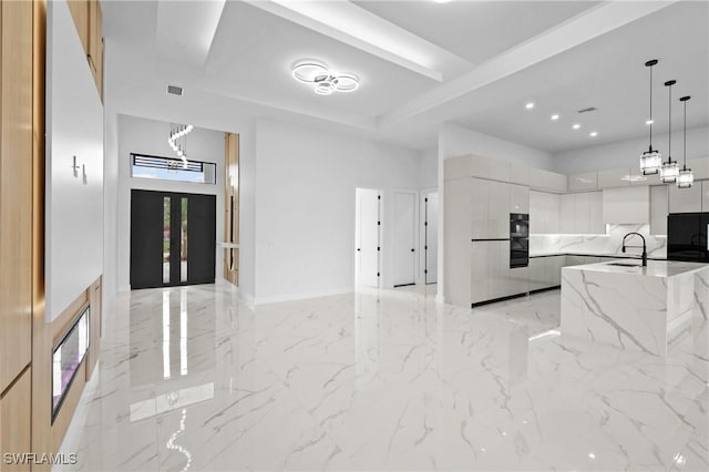 kitchen with sink, light stone countertops, white cabinets, black fridge, and decorative light fixtures