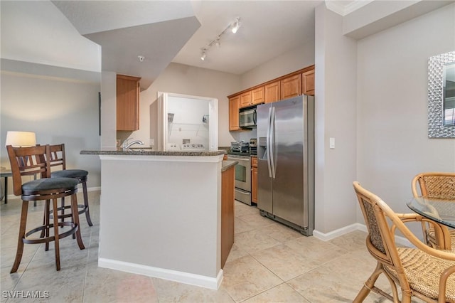 kitchen with a peninsula, a kitchen breakfast bar, baseboards, appliances with stainless steel finishes, and dark stone counters