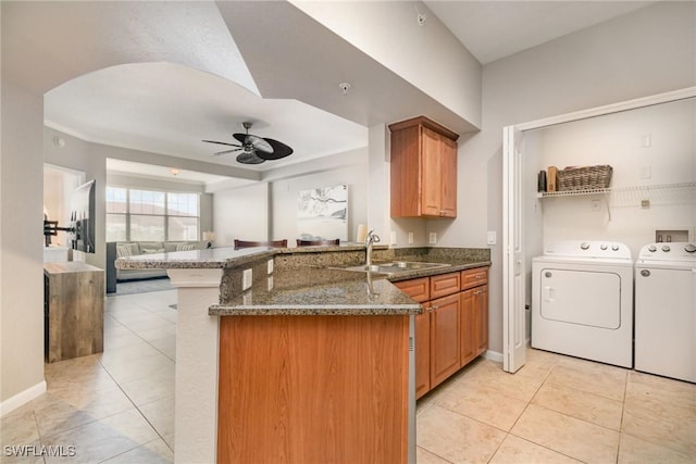 kitchen featuring a ceiling fan, a sink, separate washer and dryer, dark stone counters, and a peninsula