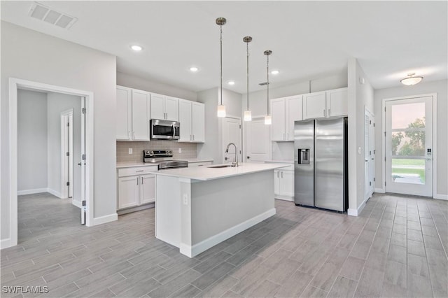 kitchen featuring pendant lighting, white cabinetry, backsplash, stainless steel appliances, and an island with sink