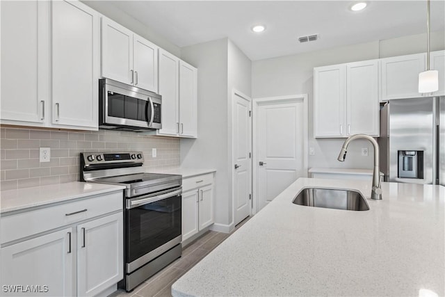 kitchen with stainless steel appliances, sink, white cabinets, and decorative light fixtures