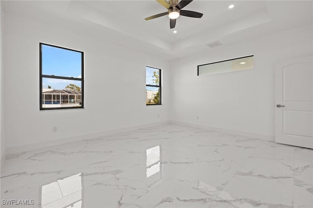 empty room featuring ceiling fan, a raised ceiling, and a wealth of natural light