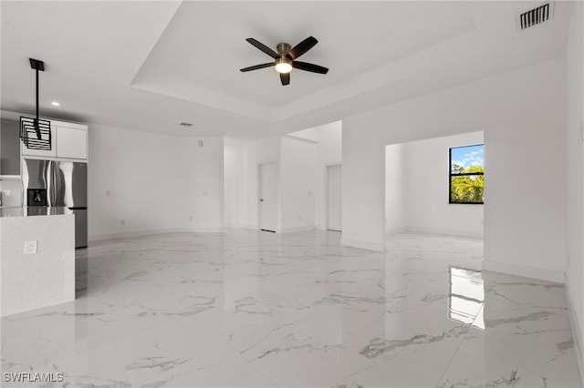 unfurnished living room featuring a raised ceiling and ceiling fan