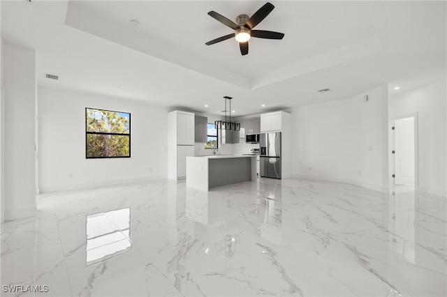 unfurnished living room featuring ceiling fan, a tray ceiling, and sink