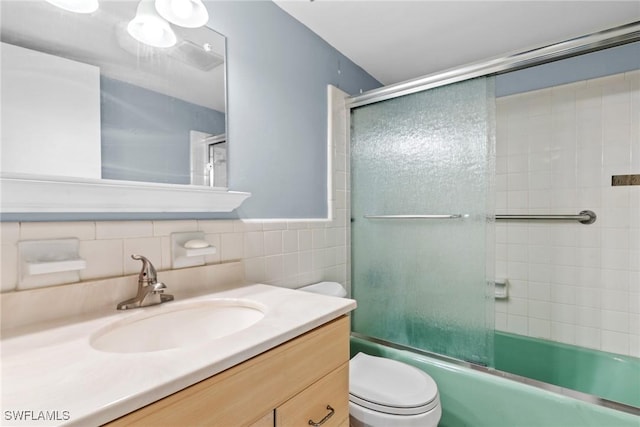 full bathroom featuring vanity, combined bath / shower with glass door, tile walls, and toilet