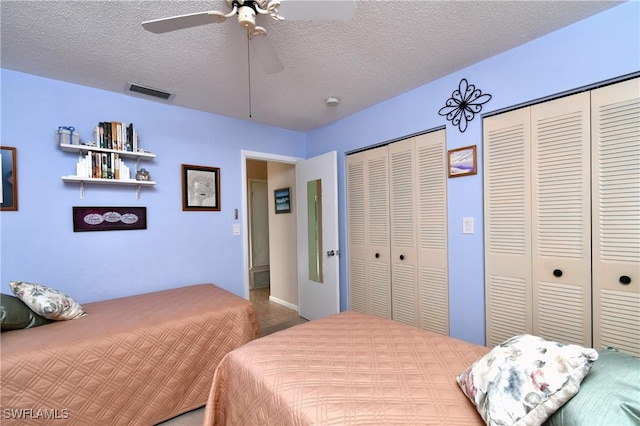 bedroom featuring ceiling fan, a textured ceiling, and two closets