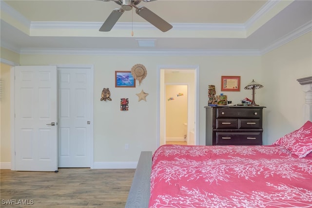 bedroom with ensuite bathroom, hardwood / wood-style flooring, ornamental molding, ceiling fan, and a tray ceiling