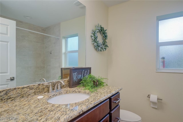 bathroom with tiled shower, vanity, and toilet