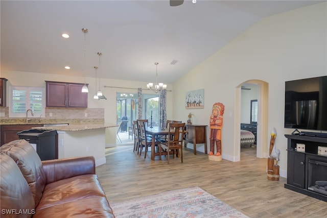 living room with an inviting chandelier, high vaulted ceiling, sink, and light hardwood / wood-style floors