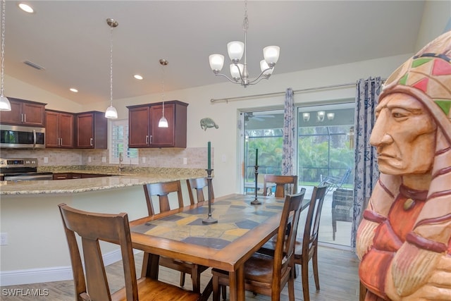 dining area with an inviting chandelier, lofted ceiling, and light hardwood / wood-style flooring