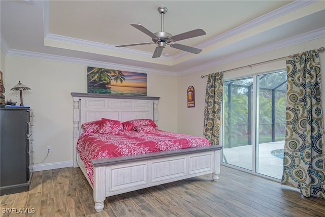 bedroom with crown molding, hardwood / wood-style floors, a tray ceiling, and access to outside